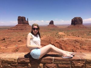 Jess Buck is sat on a wall with the backdrop of Monument Valley